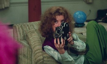 Movie still from “Lions Love (... and Lies)” (1969), directed by Agnès Varda – A woman sitting on a couch holding a camera; Medium shot, High angle