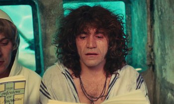 Movie still from “Lions Love (... and Lies)” (1969), directed by Agnès Varda – A man with long curly hair is sitting in a chair; Close Up shot, Low angle