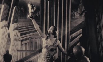 Movie still from “Lions Love (... and Lies)” (1969), directed by Agnès Varda – A woman in a dress holding up a trophy; Medium shot, Low angle