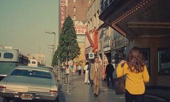 Movie still from “Lions Love (... and Lies)” (1969), directed by Agnès Varda – A man walking down a street next to a building; Extreme Wide shot, Low angle