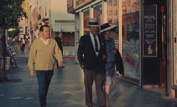 Movie still from “Lions Love (... and Lies)” (1969), directed by Agnès Varda – A man in a suit and hat walking down a street; Wide shot, High angle