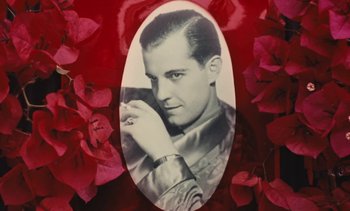 Movie still from “Lions Love (... and Lies)” (1969), directed by Agnès Varda – An old photo of a man holding a cell phone in front of some flowers; Close Up shot, High angle