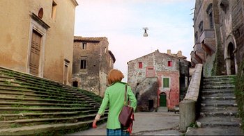 Movie still from “Lisa and the Devil” (1973), directed by Mario Bava – A woman in a green jacket walking down a street; Extreme Wide shot, Low angle