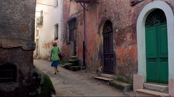 Movie still from “Lisa and the Devil” (1973), directed by Mario Bava – A woman walking down a street past a building; Wide shot, High angle
