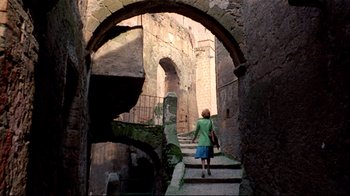 Movie still from “Lisa and the Devil” (1973), directed by Mario Bava – A woman walking down a set of stairs in an alley way; Wide shot, High angle