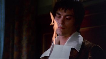 Movie still from “Lisa and the Devil” (1973), directed by Mario Bava – A man in a white dress shirt and a white tie is burning paper; Close Up shot, Low angle