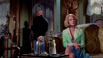 Movie still from “Lisa and the Devil” (1973), directed by Mario Bava – A woman sitting on a couch next to a man in a suit; Medium shot, Over the shoulder angle
