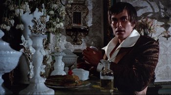Movie still from “Lisa and the Devil” (1973), directed by Mario Bava – A man sitting at a table with a plate of food in front of him; Medium shot, Low angle