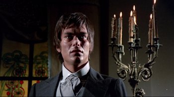 Movie still from “Lisa and the Devil” (1973), directed by Mario Bava – A man wearing a suit and tie standing in front of candles in a room; Close Up shot, Low angle
