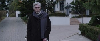Movie still from “Wish Upon” (2017), directed by John R. Leonetti – An older man wearing a black coat and a gray scarf; Medium shot, Low angle