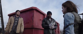 Movie still from “Wish Upon” (2017), directed by John R. Leonetti – A man standing in front of a red dumpster; Medium shot, Low angle