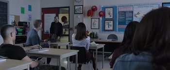 Movie still from “Wish Upon” (2017), directed by John R. Leonetti – A woman sitting at a table in a classroom; Wide shot, Over the shoulder angle
