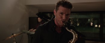 Movie still from “Wish Upon” (2017), directed by John R. Leonetti – A man holding a saxophone while standing in a room; Close Up shot, Over the shoulder angle