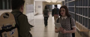 Movie still from “Wish Upon” (2017), directed by John R. Leonetti – A woman holding a tablet standing in front of a group of people in a hallway; Medium shot, Over the shoulder angle