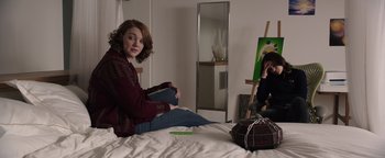 Movie still from “Wish Upon” (2017), directed by John R. Leonetti – A woman sitting on top of a bed next to a painting; Medium shot, Over the shoulder angle