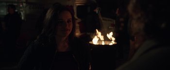 Movie still from “Wish Upon” (2017), directed by John R. Leonetti – A woman standing in front of an open fire pit; Close Up shot, Over the shoulder angle