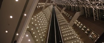 Movie still from “Wish Upon” (2017), directed by John R. Leonetti – An escalator with lights going up the side of it; Extreme Wide shot, Overhead angle