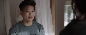 Movie still from “Wish Upon” (2017), directed by John R. Leonetti – A young man is smiling while sitting in front of a window; Close Up shot, Over the shoulder angle