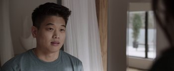 Movie still from “Wish Upon” (2017), directed by John R. Leonetti – A young asian man in front of a white curtain; Close Up shot, Over the shoulder angle