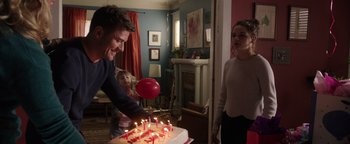 Movie still from “Wish Upon” (2017), directed by John R. Leonetti – A man and a woman standing in front of a birthday cake; Medium shot, Over the shoulder angle