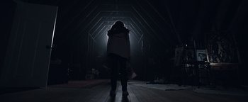 Movie still from “Wish Upon” (2017), directed by John R. Leonetti – A person standing in a dark room with a light shining on them; Wide shot, Low angle