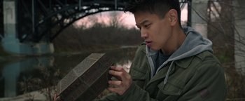 Movie still from “Wish Upon” (2017), directed by John R. Leonetti – A young man holding an object in front of a bridge; Close Up shot, High angle