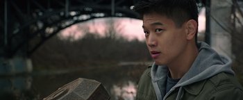 Movie still from “Wish Upon” (2017), directed by John R. Leonetti – A young man holding a box in front of a body of water; Close Up shot, Over the shoulder angle
