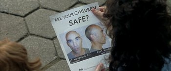 Movie still from “Little Children” (2006), directed by Todd Field – A person holding a poster of a man with bald head; Extreme Close Up shot, Overhead angle