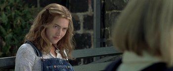 Movie still from “Little Children” (2006), directed by Todd Field – A woman sitting on top of a wooden bench next to a brick wall; Close Up shot, Over the shoulder angle