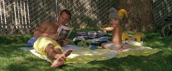 Movie still from “Little Children” (2006), directed by Todd Field – A man and a child sitting in the grass reading; Medium shot, High angle