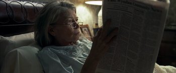 Movie still from “Little Children” (2006), directed by Todd Field – An older woman reading a newspaper in a dark room; Close Up shot, Over the shoulder angle