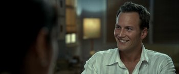 Movie still from “Little Children” (2006), directed by Todd Field – A man smiling while sitting in a room; Close Up shot, Over the shoulder angle