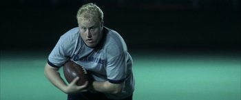 Movie still from “Little Children” (2006), directed by Todd Field – A man holding a football while standing on a field at night; Close Up shot, High angle