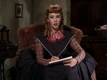 Movie still from “Little Women” (1949), directed by Mervyn LeRoy – A woman sitting in a chair writing on a piece of paper; Medium shot, Over the shoulder angle