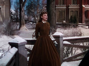 Movie still from “Little Women” (1949), directed by Mervyn LeRoy – A woman in a brown dress standing in the snow near a wooden fence; Medium shot, Low angle