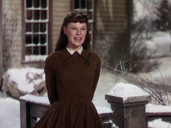 Movie still from “Little Women” (1949), directed by Mervyn LeRoy – A woman in a brown dress standing in front of a house; Medium shot, Low angle