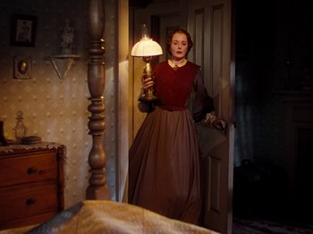 Movie still from “Little Women” (1949), directed by Mervyn LeRoy – A woman standing in front of a mirror holding a lamp; Medium shot, High angle