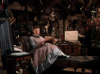 Movie still from “Little Women” (1949), directed by Mervyn LeRoy – A woman sitting on a chair reading a book; Wide shot, High angle