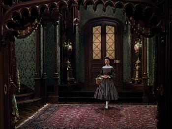 Movie still from “Little Women” (1949), directed by Mervyn LeRoy – A woman in a dress standing in front of a door; Wide shot, High angle