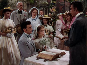 Movie still from “Little Women” (1949), directed by Mervyn LeRoy – A group of people standing around a table with a book; Medium shot, High angle