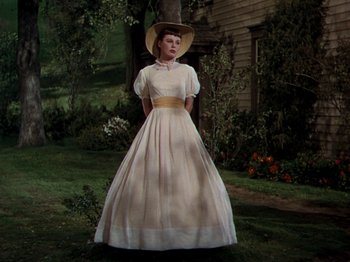 Movie still from “Little Women” (1949), directed by Mervyn LeRoy – A woman wearing a dress and a hat standing in front of a tree; Wide shot, Low angle
