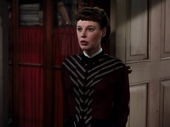 Movie still from “Little Women” (1949), directed by Mervyn LeRoy – A woman wearing a striped tie standing in front of a door; Medium shot, Low angle