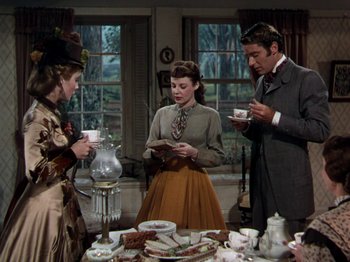 Movie still from “Little Women” (1949), directed by Mervyn LeRoy – A group of people standing around a table with plates of food on top of it; Medium shot, Over the shoulder angle