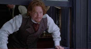 Movie still from “Little Women” (1994), directed by Gillian Armstrong – A man with a red beard and a vest leaning on a window ledge; Medium shot, Low angle