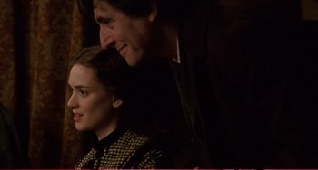 Movie still from “Little Women” (1994), directed by Gillian Armstrong – A man and a woman sitting next to each other in a dark room; Medium shot, Over the shoulder angle