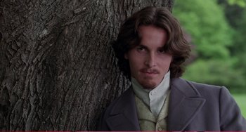 Movie still from “Little Women” (1994), directed by Gillian Armstrong – A man with long brown hair leaning against a tree; Close Up shot, High angle