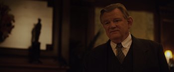 Movie still from “Live by Night” (2016), directed by Ben Affleck – An older man wearing a suit and tie in front of a window; Close Up shot, Over the shoulder angle