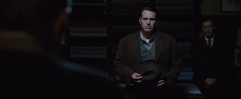 Movie still from “Live by Night” (2016), directed by Ben Affleck – A man holding a brown hat in a room; Medium shot, Over the shoulder angle