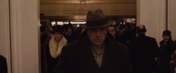 Movie still from “Live by Night” (2016), directed by Ben Affleck – A man wearing a hat standing in front of a group of people; Medium shot, Low angle