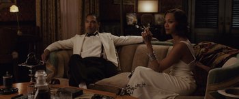 Movie still from “Live by Night” (2016), directed by Ben Affleck – A man and a woman sitting on a couch in a living room; Medium shot, Over the shoulder angle